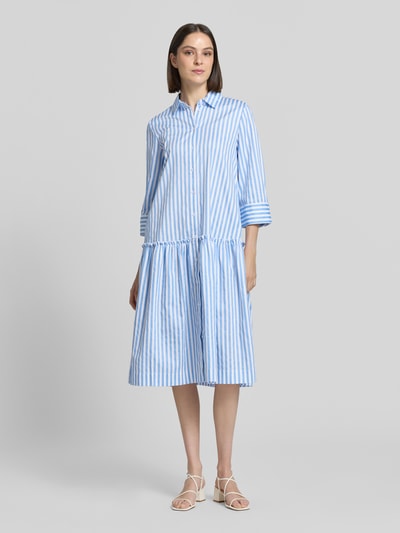 Frauenmodel trägt Relaxed Fit Hemdblusenkleid mit Rüschenbesatz von Christian Berg Woman, Reine Baumwolle, blau-weiß gestreift, Hemdblusenkragen, 3/4-Arm, durchgehende Knopfleiste, Rückenlänge 109 cm, Brustweite 49 cm, Ärmellänge 48 cm, Ganzkörperansicht von vorne.