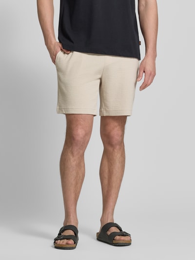 Männermodel trägt Regular Fit Sweatshorts aus Baumwoll-Mix Modell 'AUSTIN' von HUGO in Optik: Unifarben mit Waffelstruktur, seitliche Eingrifftaschen, Tunnelzug, Bundabschluss: Elastisch, Farbe Beige, Ganzkörperansicht von vorne.