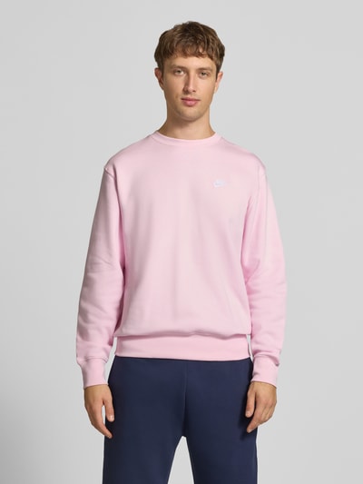 Männermodel trägt Relaxed Fit Sweatshirt aus Baumwoll-Mix von Nike in Hellrosa mit glatter Textur, dunkelblaue Hose, Ganzkörperansicht von vorne. Herren Sweatshirt von Nike.