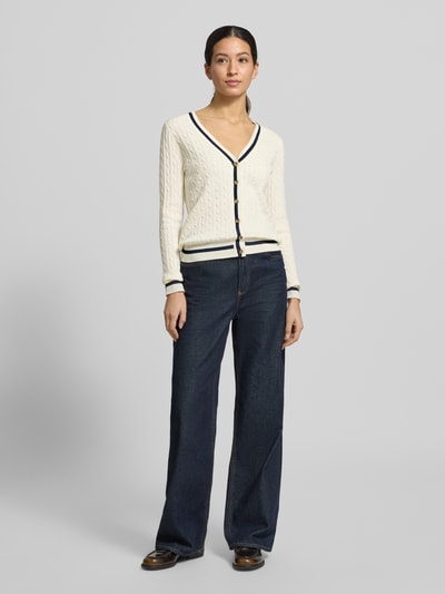 Vrouwenmodel draagt Strickjacke mit V-Ausschnitt van Christian Berg Woman, gebroken wit met donkerblauwe accenten, katoenmengsel, regular fit, geribbelde boorden, knoopsluiting, ruglengte maat S 58 cm, mouwlengte 66 cm, volledig lichaam vooraanzicht.