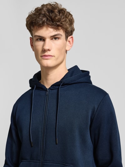 Männermodel draagt Sweatjacke met kapuze model 'BRADLEY' van Jack & Jones in donkerblauw, katoenmix, losse pasvorm, ritssluiting, kangoeroezak, ruglengte 74 cm, mouwlengte 63 cm, Nahaufnahme Oberkörper.