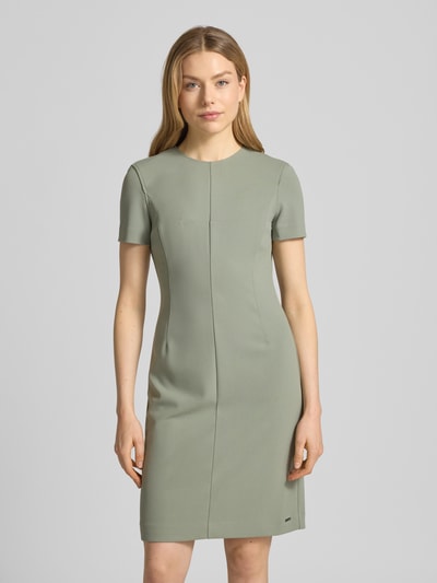 Modelka kobieca nosi 'Knielanges Etuikleid mit Rundhalsausschnitt' od Calvin Klein Womenswear, materiał z domieszką stretchu, prosty krój, długość do kolan, okrągły dekolt, długość tyłu w rozmiarze S: 92 cm, szerokość w rozmiarze S: 43 cm, długość rękawa w rozmiarze S: 19 cm, jasny odcień zieleni, gładka faktura, widok całej sylwetki z przodu.