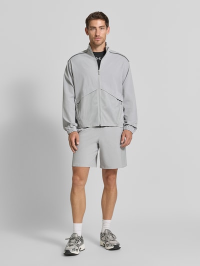 Männermodel trägt Regular fit jack met opstaande kraag Model 'Unstoppable' van Under Armour, lichtgrijs, elastische materiaalmix, elastische mouwboord, ruglengte maat M 67 cm, mouwlengte maat M 64 cm, ganzkörperaanzicht van voren.