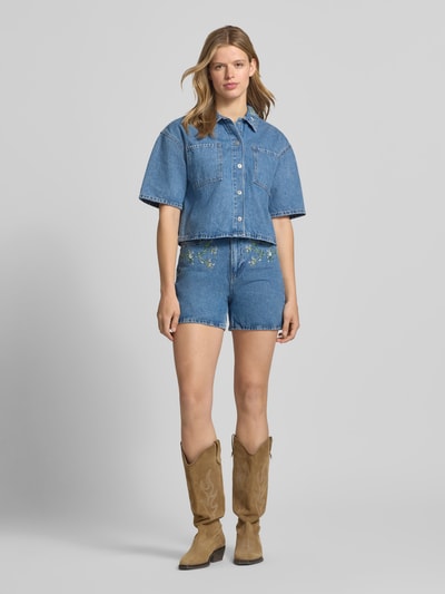 Frauenmodel trägt Boxy Fit Jeansbluse aus reiner Baumwolle Modell 'SKY' von Pieces in Denim-Optik mit Stickerei, Ganzkörperansicht von vorne.