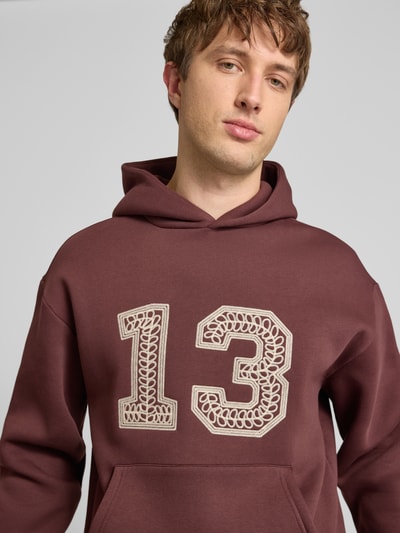 Männermodel trägt Hoodie mit Ketten-Stickerei und Känguru-Tasche von REVIEW in Braun, Baumwoll-Mix, Regular-Fit, Nahaufnahme Oberkörper.