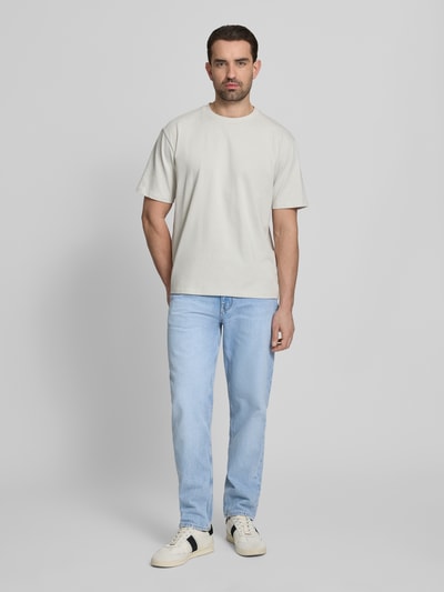 Männermodel trägt Tapered-Fit Jeans aus reiner Baumwolle Modell 'HARLEM' von Tommy Hilfiger in heller Denim-Optik, Ganzkörperansicht von vorne. 5-Pocket-Design, Regular Tapered Passform, Label-Patch, Logo-Stitching, Nieten, Gürtelschlaufen, Knopf und verdeckter Reißverschluss, strukturierte Baumwoll-Textur.