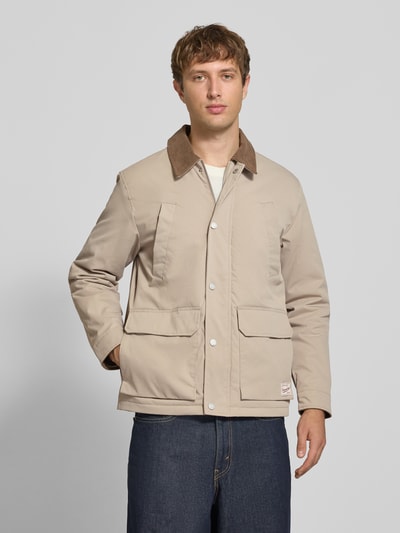 Mannenmodel draagt Regular Fit Jacke in Stiksels van JACK & JONES in beige met opgestikte zakken, logopatch, platte kraag in corduroy look, ganzeklich van voren.
