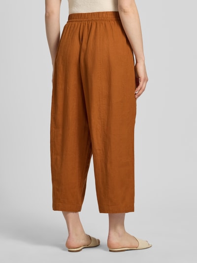Frauenmodel trägt Leinenhose in verkürzter Passform mit elastischem Bund von Christian Berg Woman aus Reinem Leinen, Wide Leg, Tunnelzug, Farbe terracotta, glatte Oberfläche, Innenbeinlänge 64 cm bei Größe 36, Ganzkörperansicht Rückansicht.