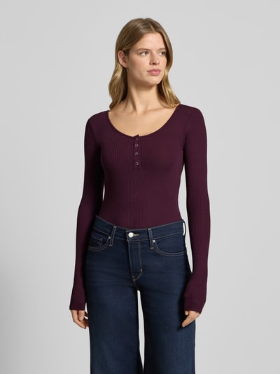 Modelka kobieca nosi Slim Fit Langarmshirt aus Baumwoll-Mix Modell 'KITTE' od Pieces, bordowy prążkowany materiał, guziki, widok całej sylwetki z przodu.