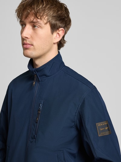 Männermodel trägt Regular Fit Bomberjacke mit Stehkragen Modell 'Parker' von Jack & Jones in Dunkelblau, Softshell, Nahaufnahme Oberkörper. Napoleontasche und elastische Abschlüsse sind sichtbar.