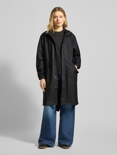 Modelka kobieca nosi czarny Regular Fit Parker z kapturem model 'Fishtail' od Rains, kieszenie z patką, elastyczne zakończenia rękawów, długość tyłu w rozmiarze S: 104 cm, szerokość ramion w rozmiarze S: 45 cm, szerokość klatki piersiowej w rozmiarze S: 55 cm, długość rękawów w rozmiarze S: 65 cm, pełen widok z przodu.