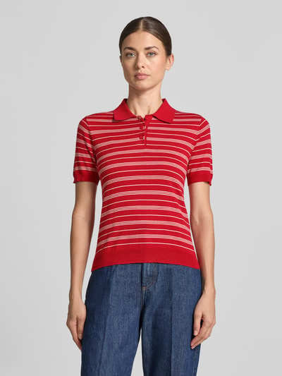 Frauenmodel trägt Slim Fit Strick-Poloshirt aus Viskose-Mix Modell 'POLVITO' von MANGO, rot mit weißen Streifen, gerippte Abschlüsse, Ganzkörperansicht von vorne.