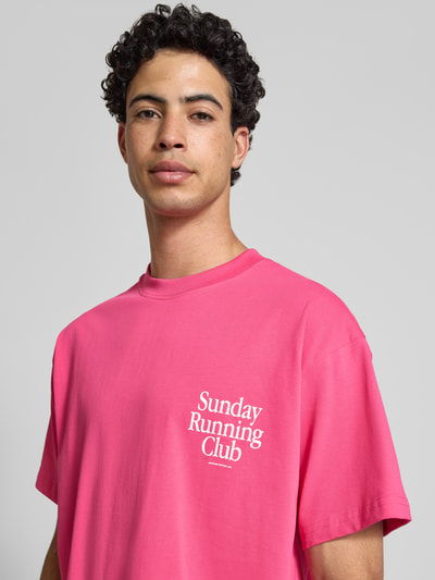 Männermodel trägt T-Shirt mit Statement-Print Modell 'Sunday Running Club' von ANOTHER COTTON LAB in Pink, reine Baumwolle, Boxy Fit, Nahaufnahme Oberkörper.