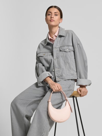 Vrouwenmodel draagt dames Handtasche aus leer met labeldetail model 'DELIZIA MINI' van FURLA, lichtroze kleur, draagband, hoofdvak met ritssluiting, schouderbandlengte 35 cm, breedte 18 cm, lengte 20 cm, diepte 3 cm, detailopname van voren.