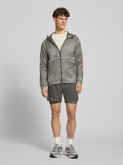 Männermodel trägt Jacke mit Reißverschlusstaschen Modell 'SABER JACKET 2.0' von HALO in Grau mit Kapuze und Logo, Regular-Fit, Ganzkörperansicht von vorne.