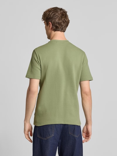 Männermodel trägt Herren T-Shirt mit Label-Detail Modell 'FILLIP' von Blend in Grün, Reine Baumwolle, Gerader-Schnitt, Rückenlänge 69 cm, Ganzkörperansicht Rückansicht.