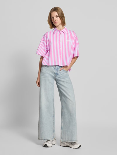 Frauenmodel trägt Cropped Bluse mit Label-Stitching Modell 'VEXTOWN' von American Vintage, rosa-weiß gestreift, Baumwolle, Ganzkörperansicht von vorne. Damen Bluse, Allover-Look, Hemdblusenkragen, Knopfleiste, Rückenlänge 55 cm, Ärmellänge 26 cm.