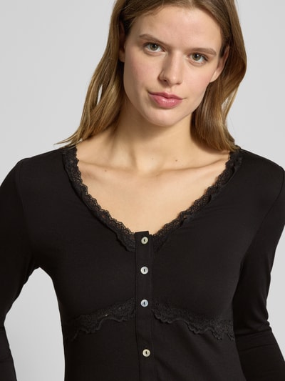 Kobieta modelka nosi Slim Fit Langarmshirt aus Viskose-Mix Modell 'SINI' od Only, czarny, koronka, dekolt V, zapięcie na guziki, krój slim fit, detal z logo, gładki materiał, półzbliżenie górnej części ciała.