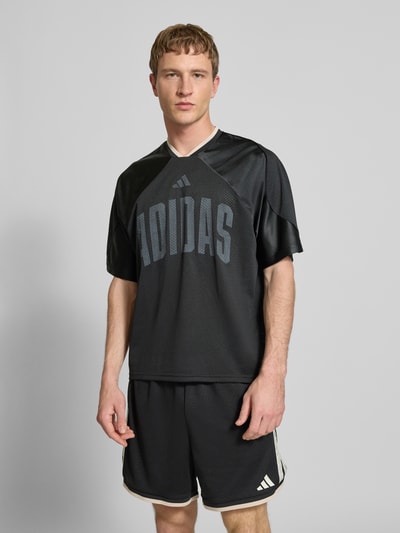 Männermodel trägt T-Shirt mit V-Ausschnitt und Logo-Print von adidas Sportswear in Schwarz, lockerer Schnitt, tonaler Logo-Print, Nahaufnahme Oberkörper.