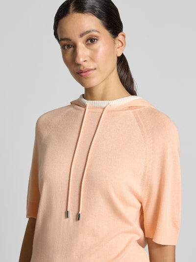 Frauenmodel trägt Relaxed Fit Hoodie aus Woll-Mix von Marc Cain in zartem Apricot, Strick-Optik, Kapuze, Halbarm, Nahaufnahme Oberkörper.