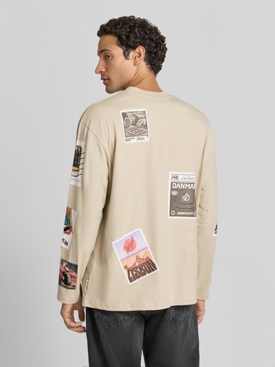 Männermodel trägt Longsleeves mit Motiv-Prints Modell 'Stamp' von Les Deux, beige mit geripptem Rundhalsausschnitt, Ganzkörperansicht Rückansicht. Baumwoll-Mix mit Stretch-Anteil, Straight Fit, Rückenlänge bei Größe M 70 cm.