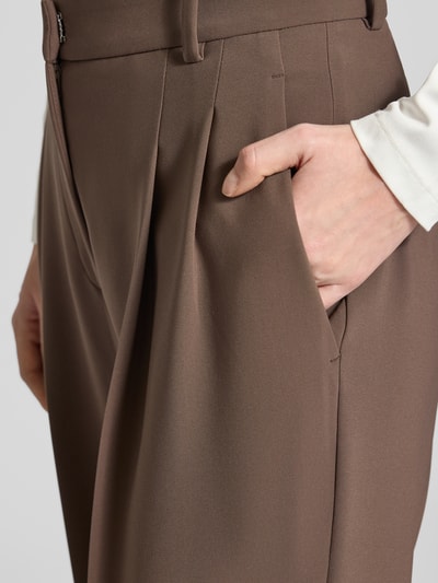 Frauenmodel trägt Wide Fit Stoffhose mit Gesäßtaschen Modell 'Emilie' von Cambio in Braun, glatte Textur, Detailaufnahme Oberschenkel. Damen Stoffhose, Bügelfalten, Haken- und Reißverschluss, Bundweite 39 cm, Innenbeinlänge 81 cm.