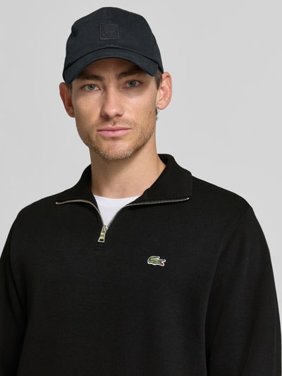 Männermodel trägt Regular Fit Troyer aus reiner Baumwolle von Lacoste in Schwarz mit Reißverschluss und Krokodil-Logo, Nahaufnahme Oberkörper. Herren Troyer von Lacoste.
