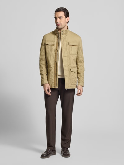Męski model nosi Jacke mit Stehkragen und Pattentaschen od Christian Berg Men w kolorze beżowym, krój regular fit, z bawełny z domieszką elastanu, kieszenie z patkami, długość tyłu w rozmiarze M: 73 cm, szerokość ramion w rozmiarze M: 43 cm, szerokość klatki piersiowej w rozmiarze M: 56 cm, długość rękawa w rozmiarze M: 67 cm, pełny widok z przodu.