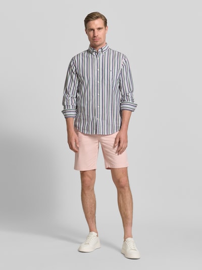 Męski model nosi Regular Fit Bermudas aus Baumwoll-Mix od Tommy Hilfiger, jasnoróżowy, gładki, bawełniany, widok całej sylwetki z przodu.