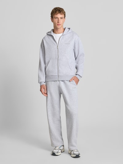 Männermodel trägt Regular Fit Sweatjacke aus Baumwoll-Mix von REVIEW in Hellgrau mit Kapuze, Känguru-Tasche und Reißverschluss, Ganzkörperansicht von vorne.