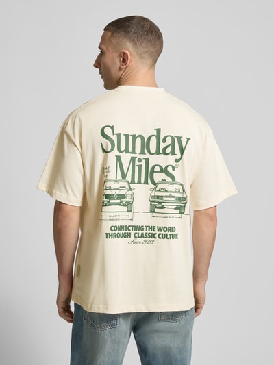 Männermodel trägt T-Shirt aus Baumwolle Modell 'Sunday Miles' von ANOTHER COTTON LAB in Creme mit grünem Print, Rückenansicht, Ganzkörperansicht Rückansicht.