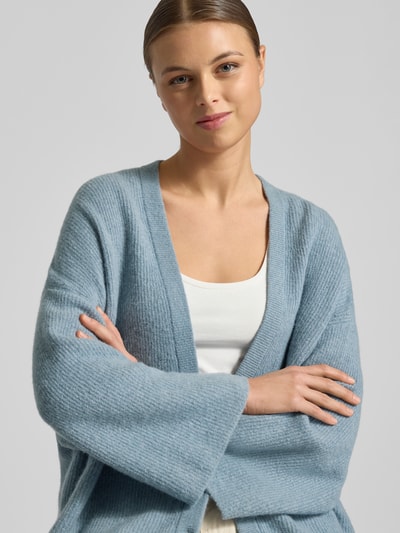 Frauenmodel trägt Relaxed Fit Cardigan mit Woll-Anteil Modell 'Damsville' von American Vintage in hellblauer Strick-Optik, Nahaufnahme Oberkörper. Material-Mix mit Woll-Anteil, V-Ausschnitt, Knopfleiste.