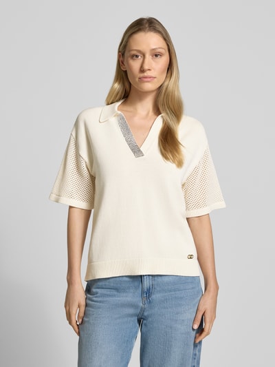 Modelka nosi Relaxed Fit Poloshirt in Strick-Optik mit Strasssteinbesatz von LIU JO SPORT z bawełny, krój relaxed fit, obszycie z kamieni stras, imitacja dzianiny, perforowanie, z krótkim rękawem, kolor ecru, długość tyłu 63 cm, długość rękawów 22 cm, przód, zbliżenie na górną część ciała.