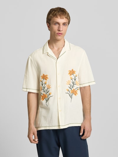 Męski model nosi Relaxed Fit Freizeithemd mit Motiv-Stitching od REVIEW, bawełniany miks, krój relaxed fit, kołnierz rewersowy, zapięcie na guziki, haft z motywem, długość pleców w rozmiarze M: 72 cm, szerokość ramion w rozmiarze M: 45 cm, długość rękawa w rozmiarze M: 30 cm, kremowy materiał z żółtymi i zielonymi detalami, widok całej sylwetki z przodu.