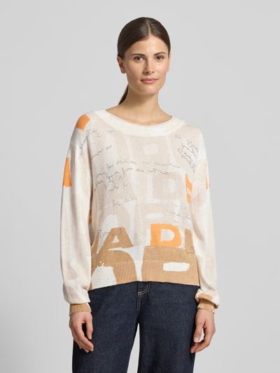 Frauenmodel trägt Pullover mit Strasssteinbesatz von monari in Beige mit Schrift, Baumwoll-Mix, Gerader-Schnitt, Rundhalsausschnitt, Rückenlänge 50 cm, Ärmellänge 58 cm, Ganzkörperansicht von vorne.