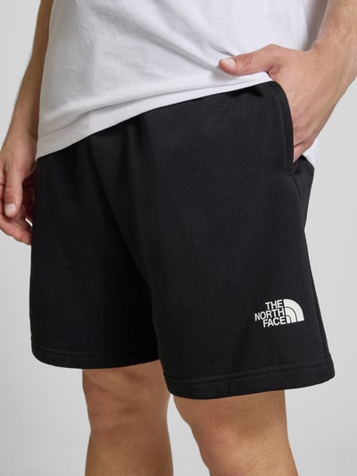 Männermodel trägt Shorts mit Logo von The North Face aus Baumwoll-Mix in Schwarz, Regular-Fit, sichtbarer elastischer Bund, Nahaufnahme Oberschenkel.