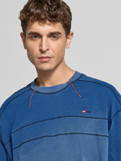 Mannenmodel draagt blauwe Diesel sweatshirt met labelstitching, mix van katoen en elastaan, recht model, ronde hals, rolzoom, detailopname bovenlichaam.