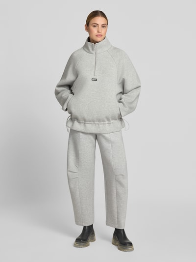 Frauenmodel trägt Hose aus Viskose-Mix von ROTATE in Hellgrau mit Relaxed-Fit, Gelegten Falten, Logo-Patch, Haken-Reißverschluss, Ganzkörperansicht von vorne.