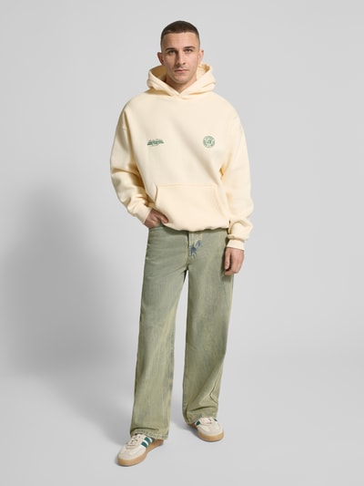 Männermodel trägt Hoodie mit Logo-Prints Modell 'Sunday Miles' von ANOTHER COTTON LAB, lockerer Schnitt, helle Farben, Ganzkörperansicht von vorne.