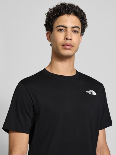 Männermodel trägt Regular Fit T-shirt aus katoenmix Modell 'EVOLUTION' van The North Face, zwart, labeldetail, ronde hals, Nahaufnahme bovenlichaam, ruglengte maat M 70 cm