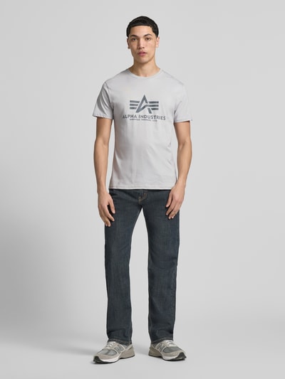 Męski model nosi t-shirt z detalem z logo model 'BASIC' od Alpha Industries, bawełna, prosty krój, okrągły dekolt, długość tyłu w rozmiarze M: 69 cm, całkowity widok z przodu