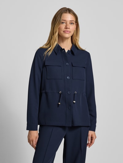 Kobiece model prezentuje Regular Fit Longblazer mit Brustpattentaschen von s.Oliver BLACK LABEL, granatowy, gładka faktura, krój regular fit, umlegekragen, długość longline, tunelik w talii, zapięcie na pojedynczy rząd guzików, długie rękawy z mankietami, kieszenie z patkami na piersi, widok całej sylwetki z przodu.