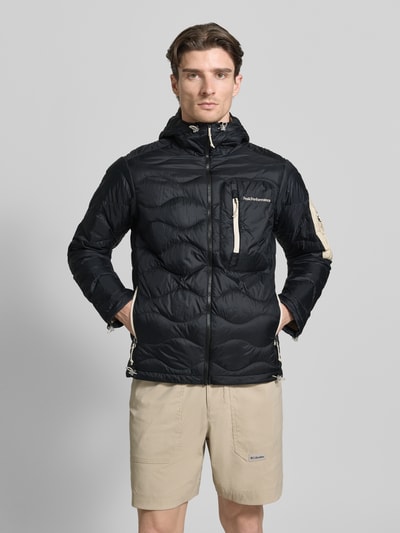 Männermodel trägt Regular Fit Jacke in Stepp-Optik mit Logo-Stitching von Peak Performance in Schwarz mit Kapuze und Eingrifftaschen, Ganzkörperansicht von vorne. Rückenlänge 71 cm, Schulterbreite 47 cm, Brustweite 56 cm, Ärmellänge 67 cm.