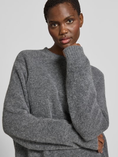 Frauenmodel trägt Pullover in Strick-Optik aus Alpaka-Mix von black palms, Relaxed-Fit, Rundhalsausschnitt, elastische Ärmelabschlüsse, graue Farbe, weiche Textur, Damen Pullover, Rückenlänge 62 cm bei Größe S, Nahaufnahme Oberkörper.