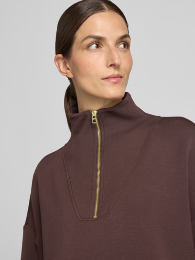 Frauenmodel trägt Regular Fit Sweatshirt aus Viskose-Mix Modell 'Hawley' von VARLEY, braune Farbe, goldener Reißverschluss, Nahaufnahme Oberkörper. Elastischer Viskose-Mix, Troyer-Kragen, elastische Abschlüsse.
