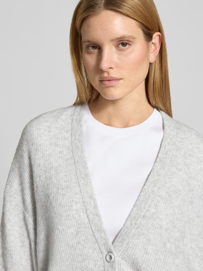 Frauenmodel trägt Relaxed Fit Cardigan mit Woll-Anteil Modell 'Damsville' von American Vintage in Hellgrau, Stricktextur, Nahaufnahme Oberkörper.