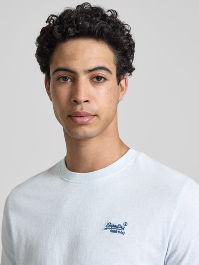 Männermodel trägt Regular Fit T-Shirt mit Logo-Stitching von Superdry aus reiner Baumwolle, hellblau, Rundhalsausschnitt, Nahaufnahme Oberkörper.