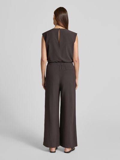 Kobiece modelka nosi kombinezon Relaxed Fit Jumpsuit mit V-Ausschnitt Modell 'Charlou' od Someday, elastyczna mieszanka materiałów, krój relaxed fit, dekolt w serek, bez rękawów, taliowany, wpuszczane kieszenie, długość tyłu w rozmiarze 36: 44 cm, szerokość w rozmiarze 36: 52 cm, całkowita długość w rozmiarze 36: 146 cm, długość wewnętrzna nogawki w rozmiarze 36: 71 cm, kolor ciemnoszary, proste szerokie nogawki, miękka tekstura, całkowity widok z tyłu
