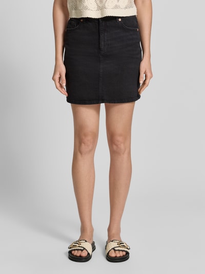 Frauenmodel trägt Regular Fit Jeansrock aus Baumwoll-Mix Modell 'TESSA' von Vero Moda in schwarzer Denim-Optik mit 5-Pocket-Design, Ganzkörperansicht von vorne.