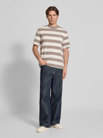 Mannenmodel draagt Regular Fit T-shirt uit katoenmix van Calvin Klein Jeans met all-over motief, gestreept patroon, logo-stitching detail, ronde hals, korte mouw, regular fit pasvorm, kleur beige-wit-bruin Ganzkörperansicht von vorne.